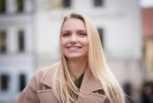 A cheerful adult woman with blonde hair smiling warmly outdoors.